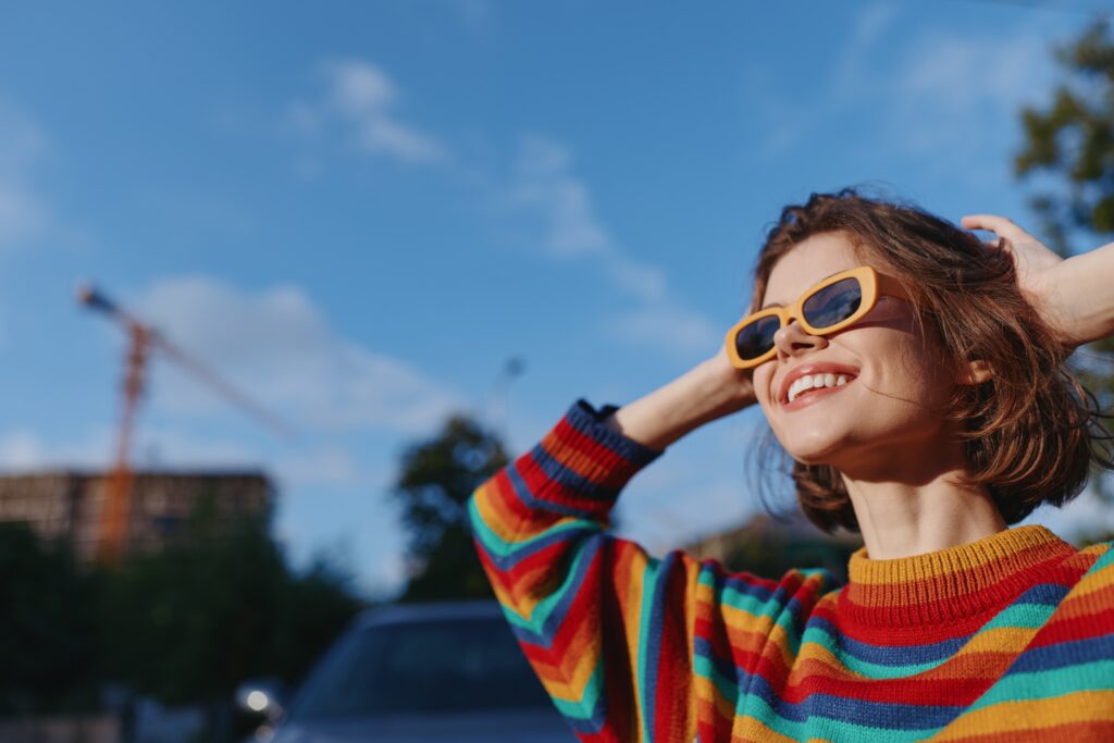 woman,smiling,in,a,colorful,striped,sweater,and,yellow,sunglasses,