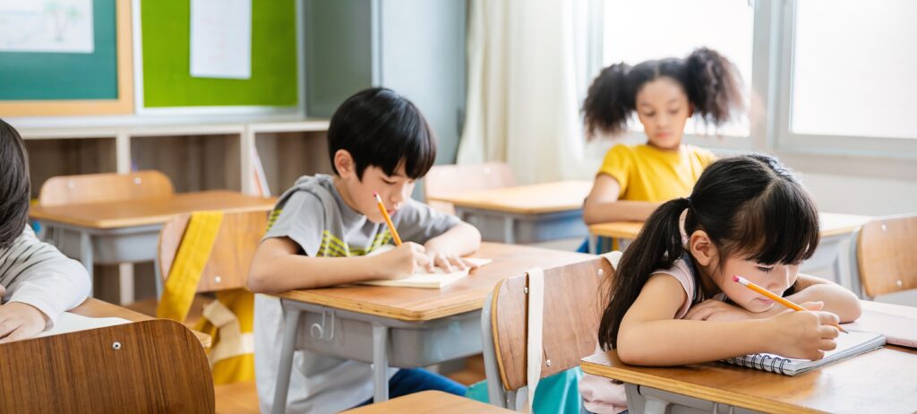 portrait,of,little,pupil,writing,at,desk,in,classroom,at